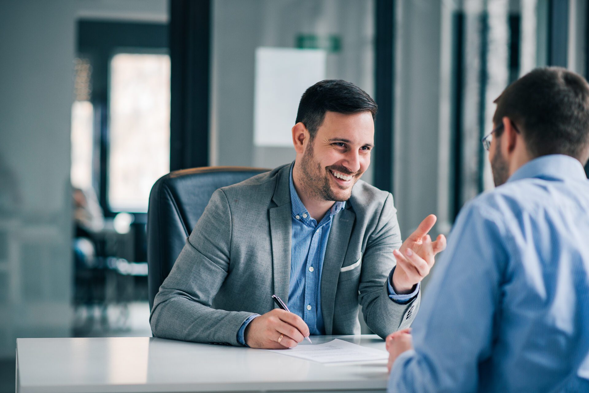 Homme souriant en costume échangeant avec un interlocuteur à son bureau lors d'un entretien.