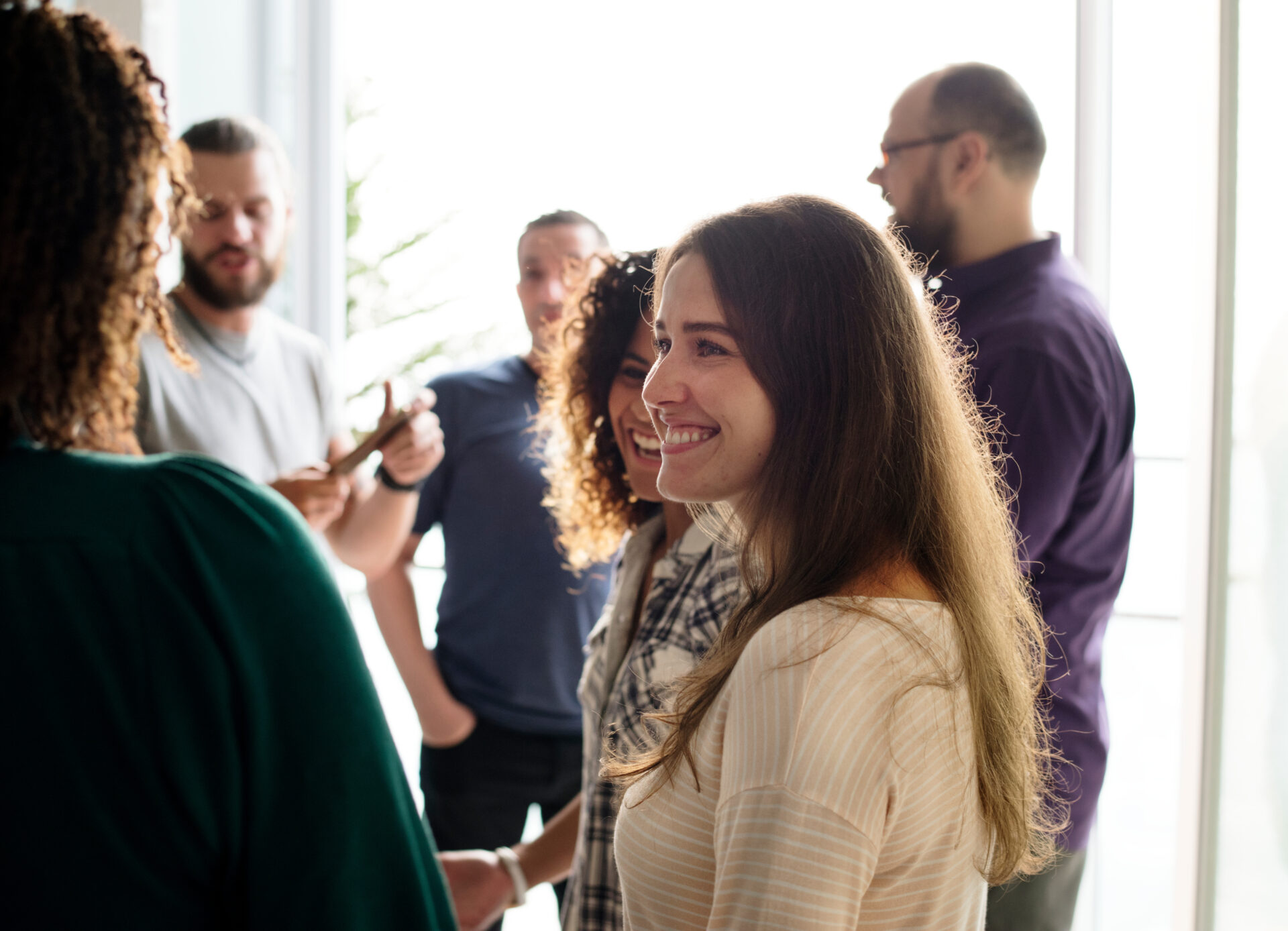 Groupe de collaborateurs souriants échangeant dans un bureau à contre-jour.
