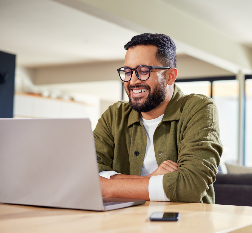 Homme souriant utilisant un ordinateur portable sur une table dans un intérieur lumineux.