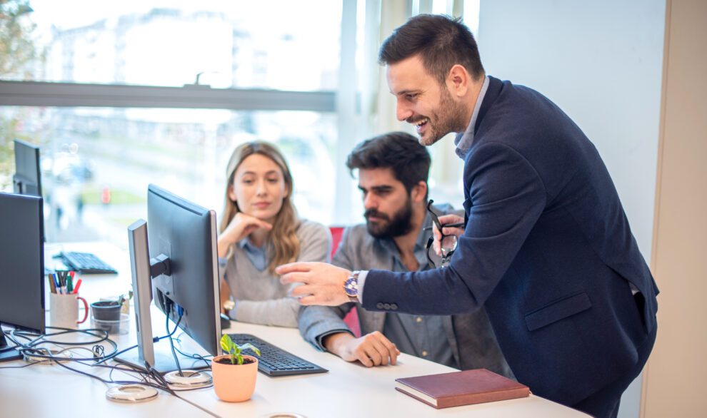 Trois collaborateurs regardant ensemble un écran d'ordinateur, l'un expliquant en pointant.