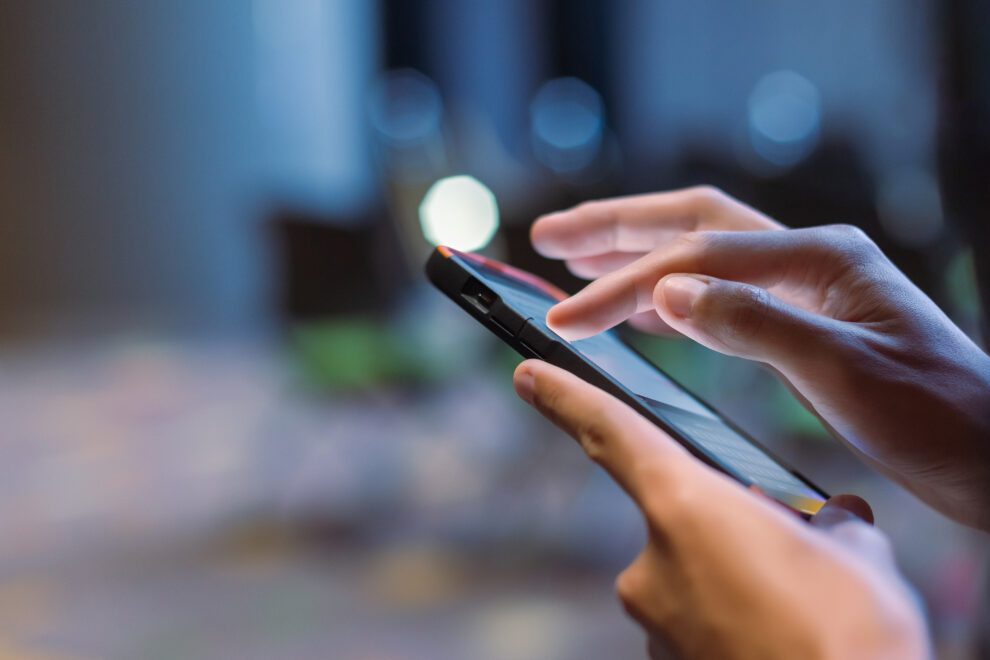 Gros plan d'une main utilisant un smartphone dans une salle de réunion en soirée.