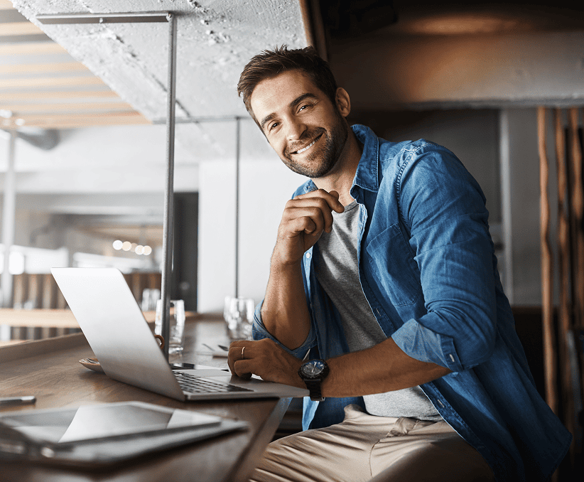 Homme souriant en chemise en jean posant devant son ordinateur portable dans un espace moderne.
