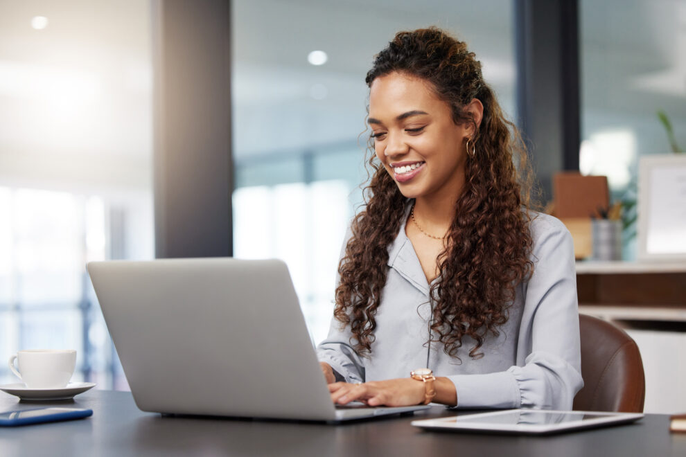 Femme souriant utilisant un ordinateur portable sur une table dans un intérieur lumineux.
