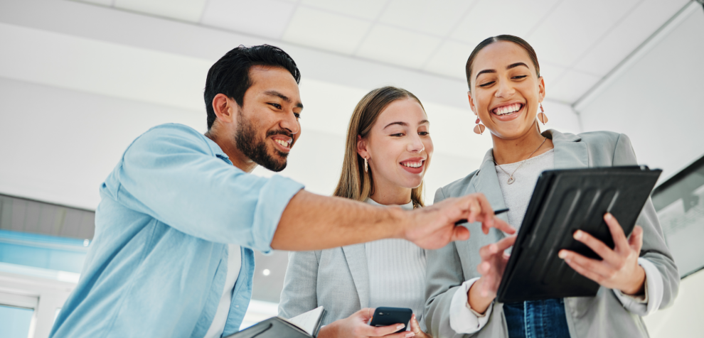 Trois professionnels souriants regardant une tablette ensemble dans un bureau.