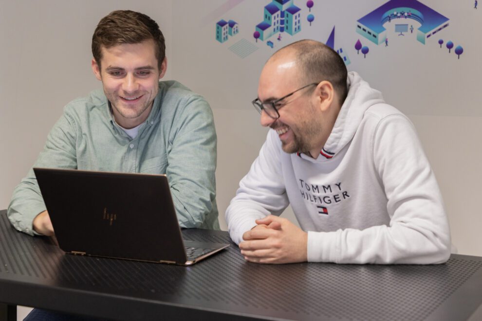 Deux collaborateurs de Twipi Group souriants devant un ordinateur portable, sous une fresque Twimm.