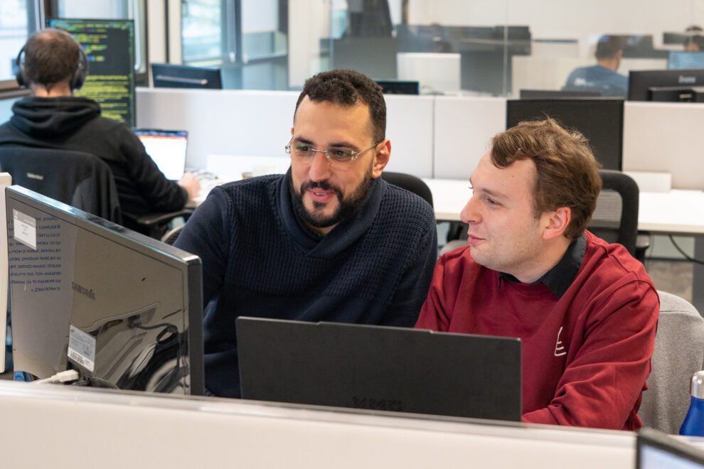 Deux développeurs de Twipi Group échangeant devant leurs écrans dans l'open space.