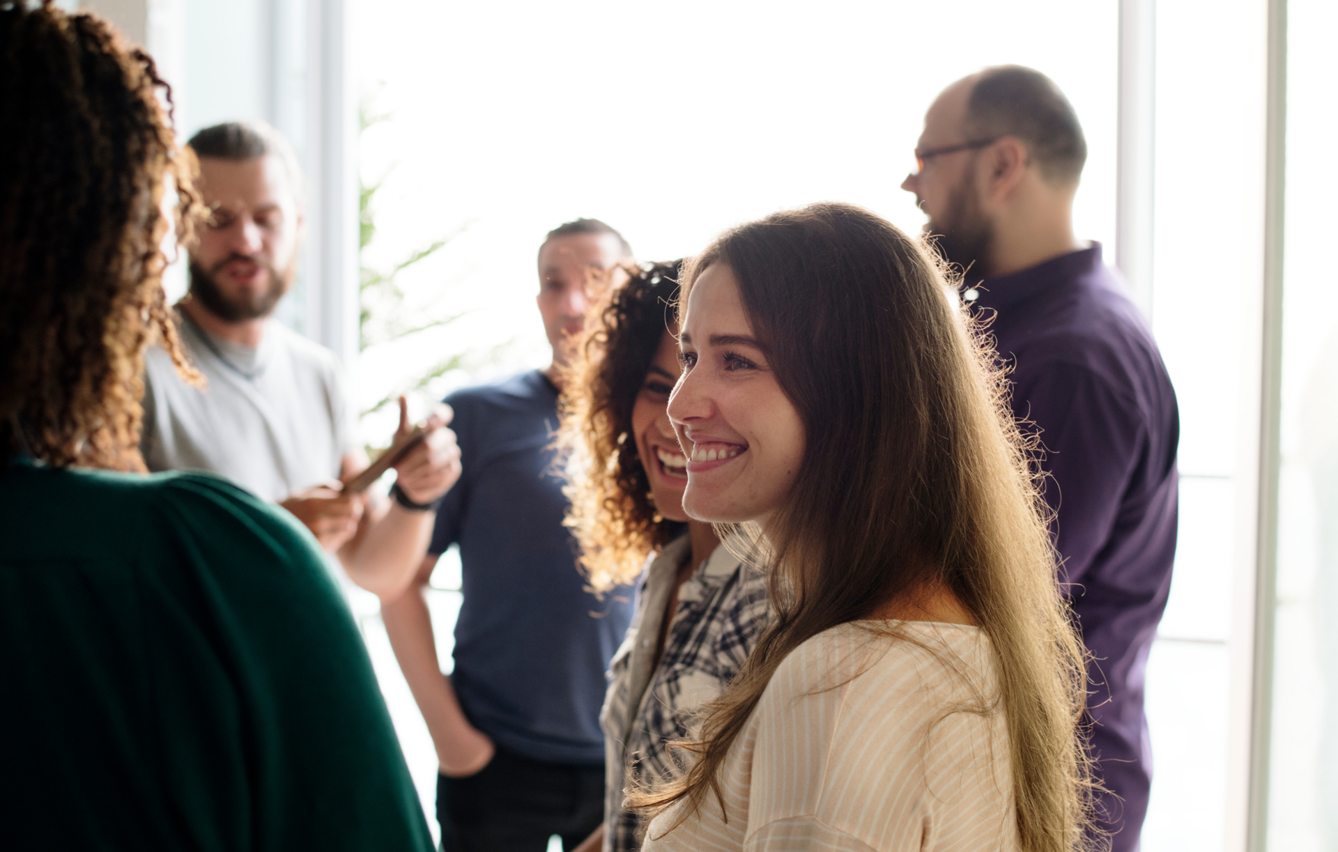 Groupe de collaborateurs souriants échangeant dans un bureau à contre-jour.