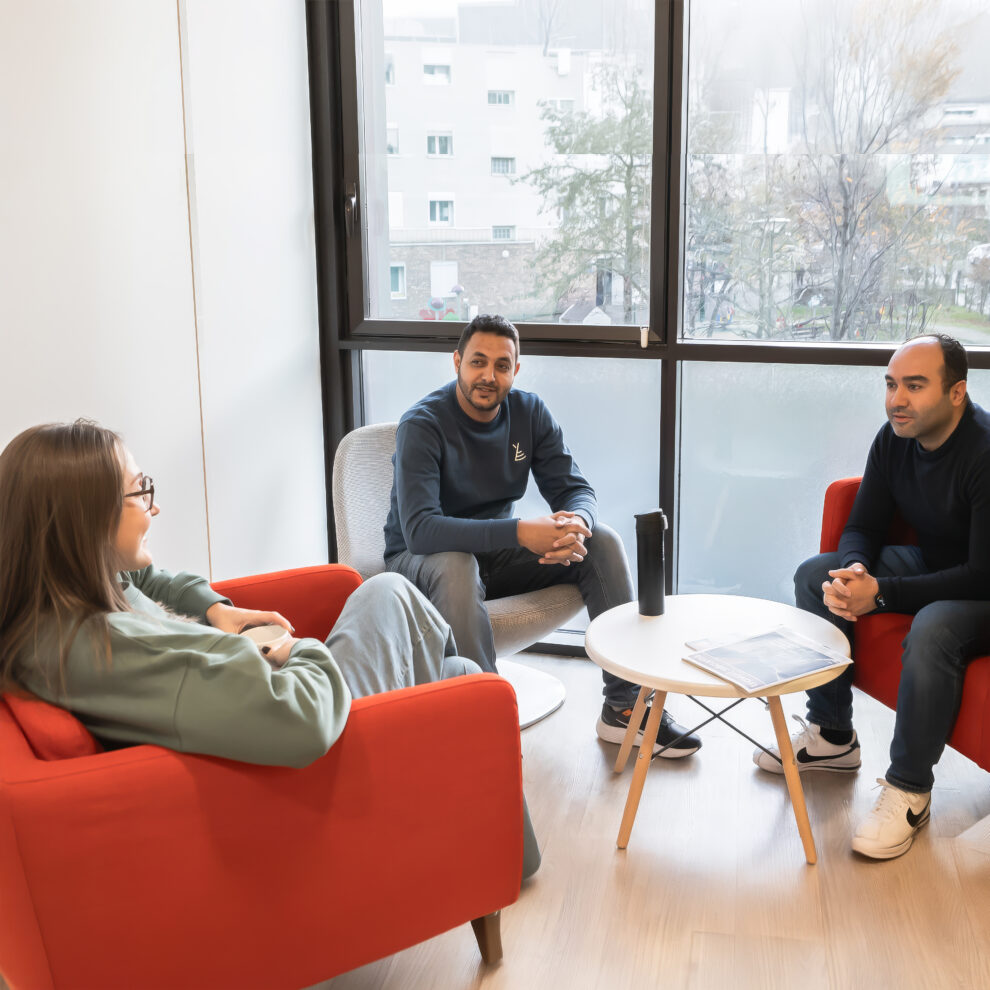 Nous rejoindre 3 Trois collaborateurs de Twipi Group en discussion dans un espace détente du bureau.